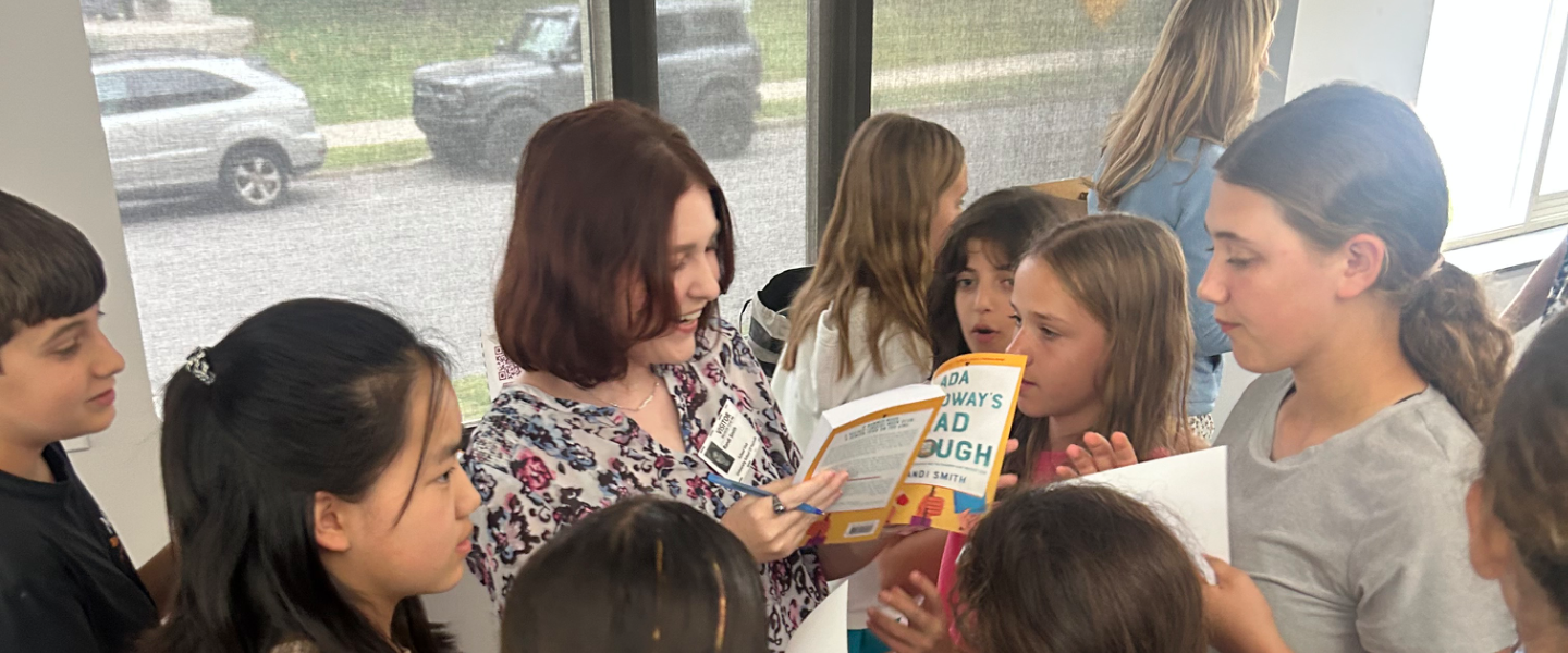 Woman author signs a book for a group of children at a literacy event.