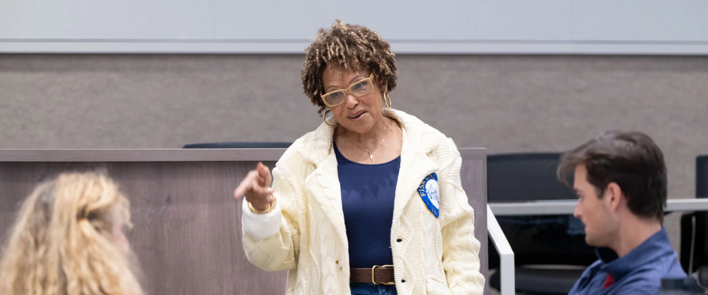 Professional woman with glasses and curly hair presenting or leading a discussion in a modern classroom.