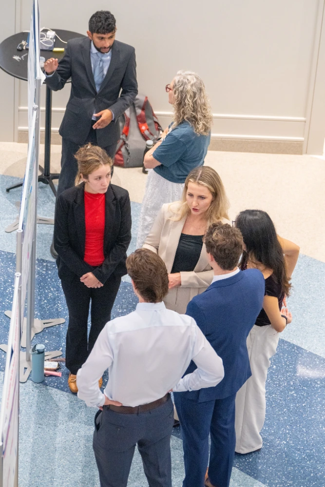 M2 student Alexandra Penney discusses her research findings with a group of Research Symposium attendees.