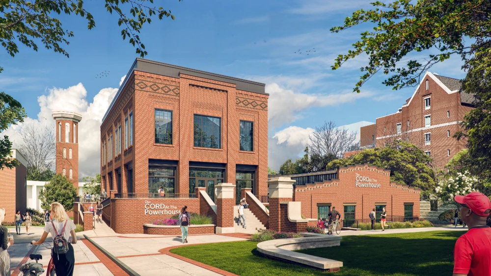 Campus scene with a brick building labeled “CORD: the Powerhouse,” students walking on pathways, and a tall tower in the background under a blue sky.