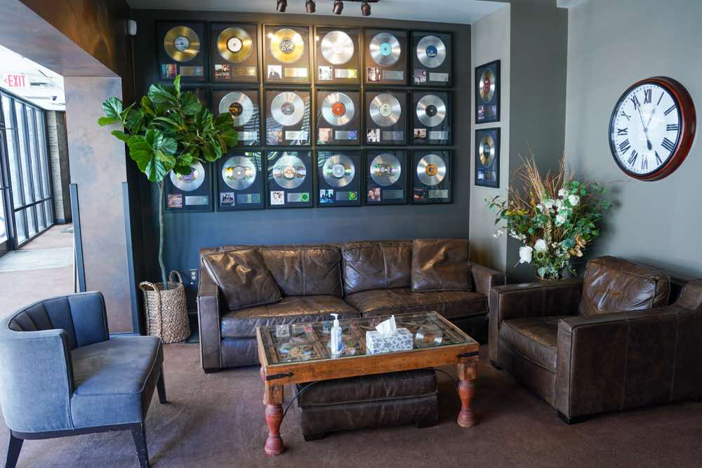 Cozy music industry lounge featuring framed gold/platinum records, plush leather seating, coffee table, and large clock.