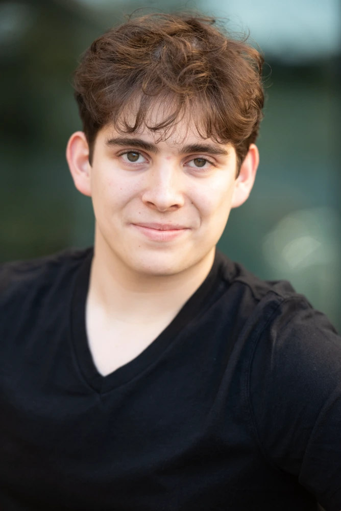 Headshot of a smiling young man with brown curly hair wearing a black v-neck shirt.