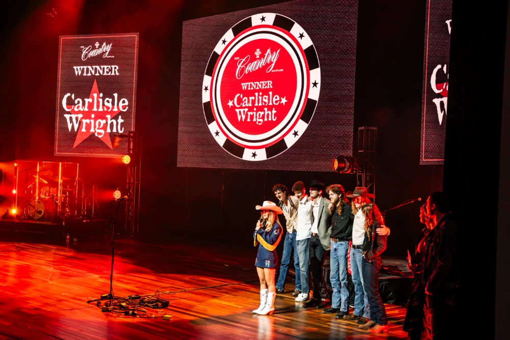 Band stands on stage during an awards announcement, with large screens behind them reading “Winner Carlisle Wright.”