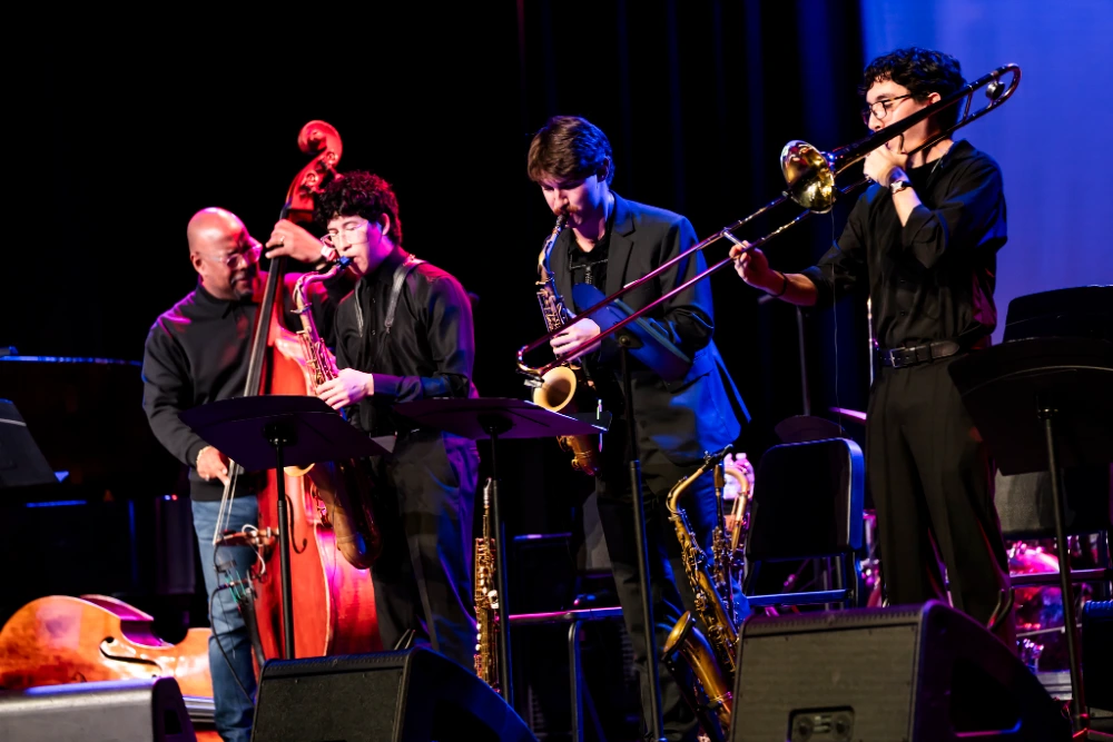 Jazz band performing live on stage with upright bass, two saxophones, and a trombone.