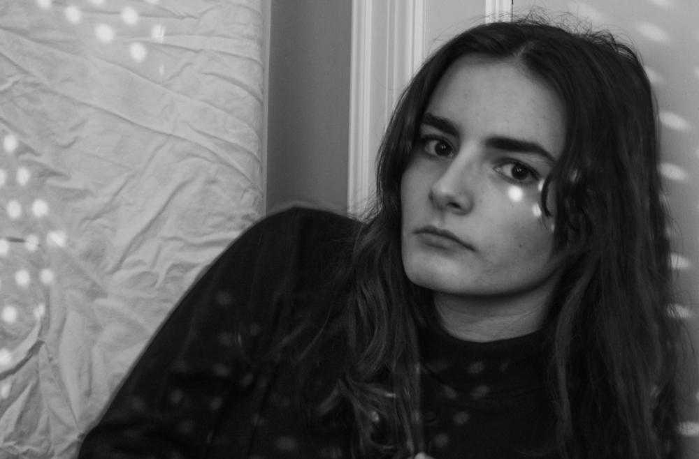 Young woman with long dark hair in a black and white portrait, dappled light on her face and a textured background.