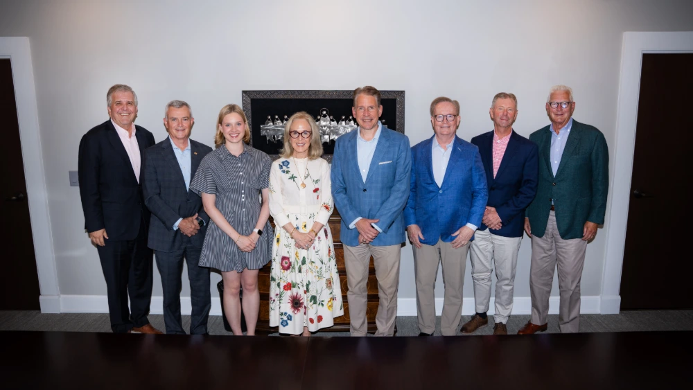 Group photo of eight business professionals, including executives and board members, in a corporate setting.