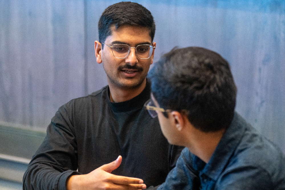 Two men in glasses having a focused discussion, one actively explaining a point to the other.
