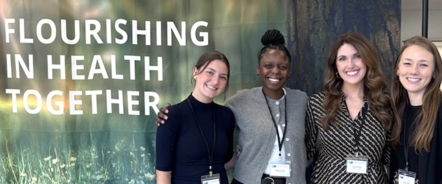 Four students smile in front of the KNN banner