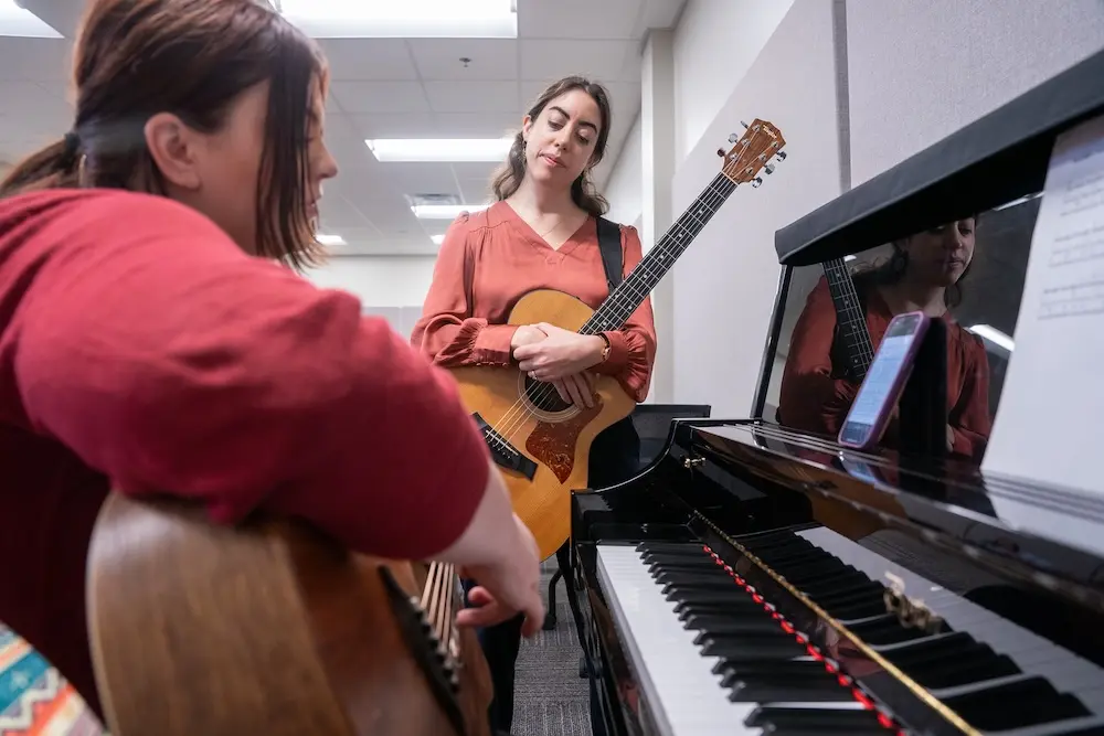a woman sitting at piano and a woman standing with a guitar