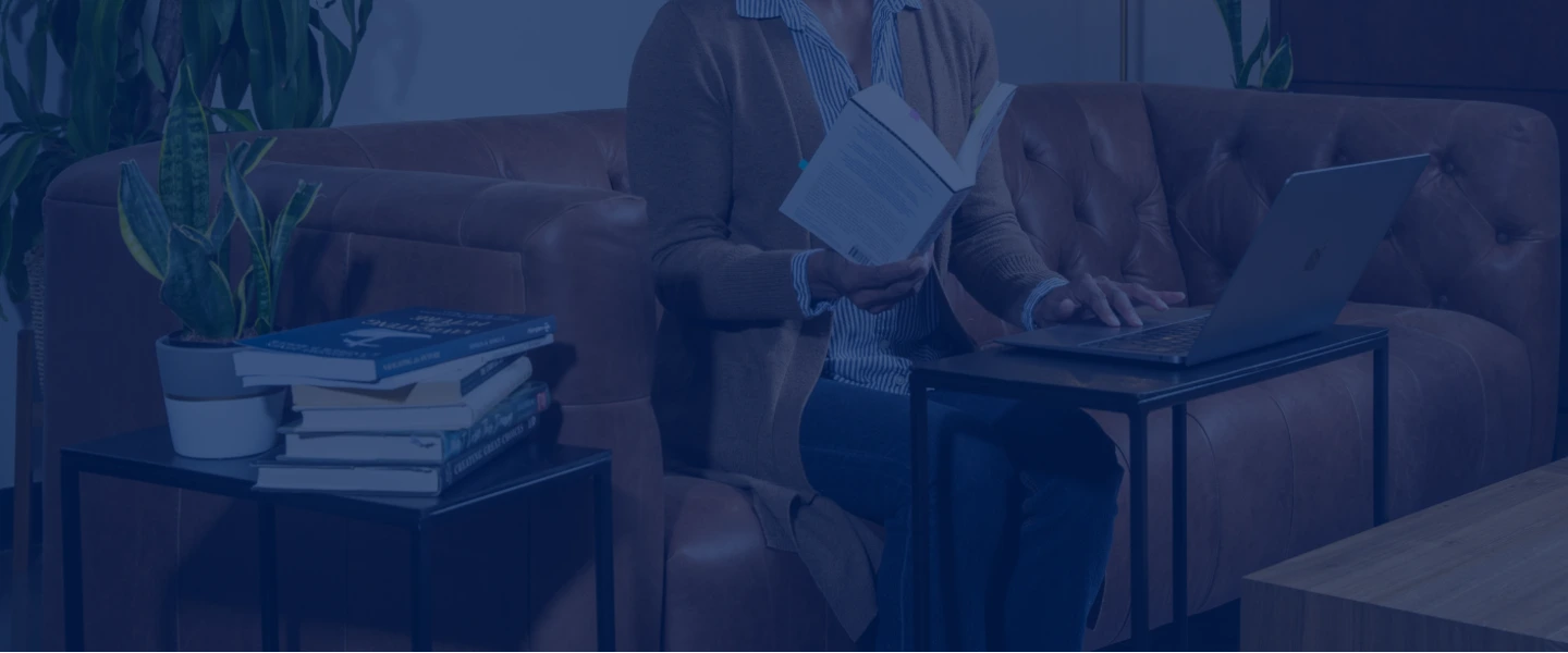 a woman sitting at a computer holding a book