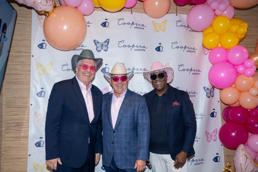 Three smiling men in cowboy hats and pink heart glasses