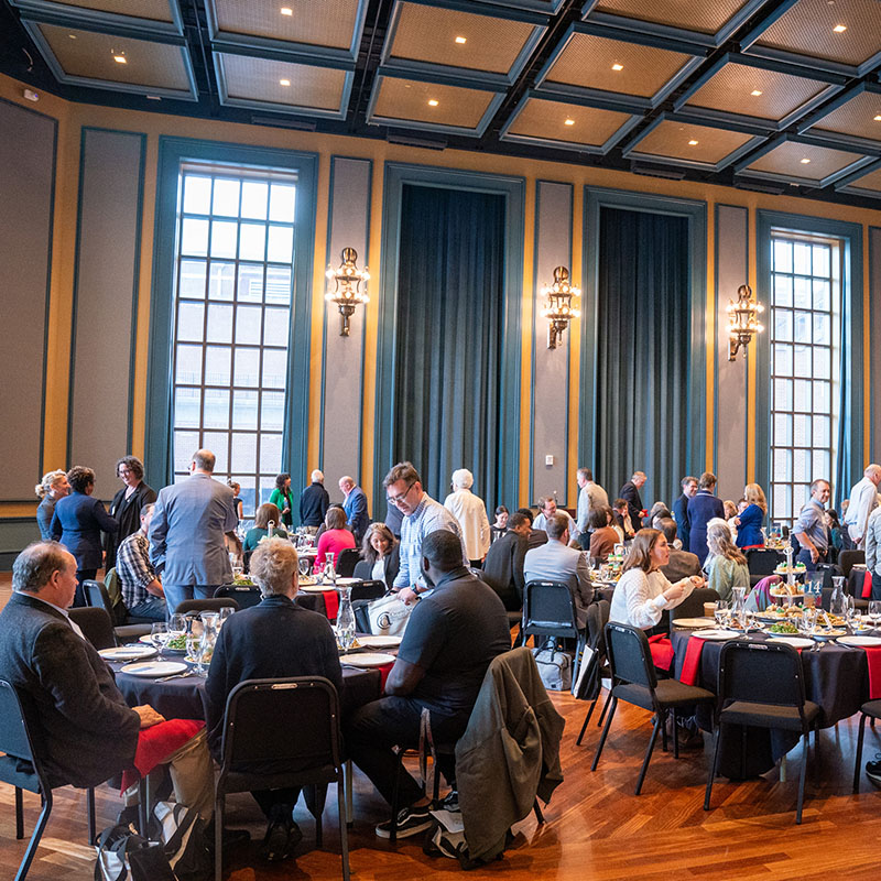 Event with people sitting at round tables in a ballroom in the Fisher Center