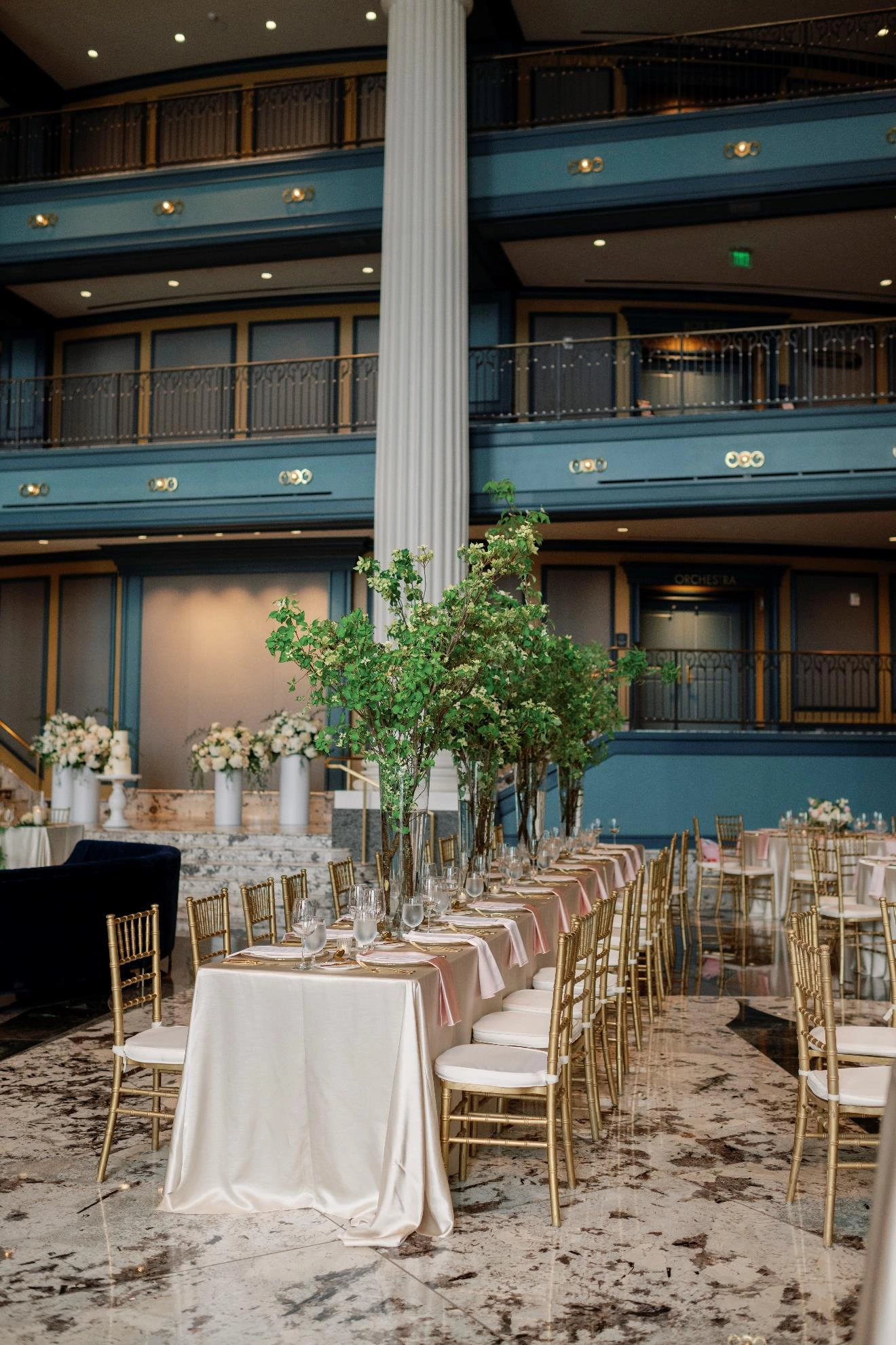 Beautifully decorated tables and chairs with pink silk for a wedding, with tall bouquets of flowers on tables in the Fisher Center lobby