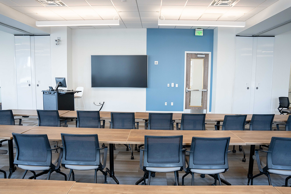Hackathon classroom full of tables and chairs set up classroom style with TV screens and podiums at the front.