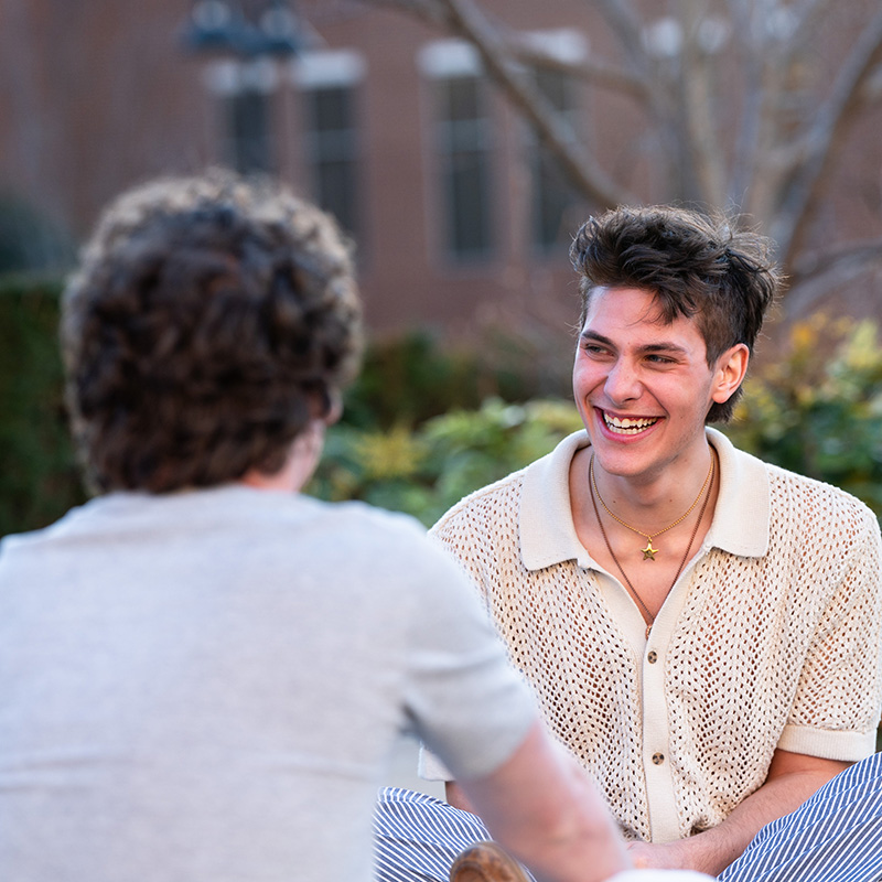 Student sitting and laughing with another student outside on a sunny day