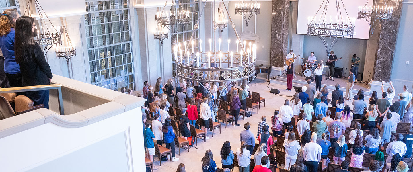 A wide angle shot of the chapel at Belmont. The room is filled with people who stand and worship.