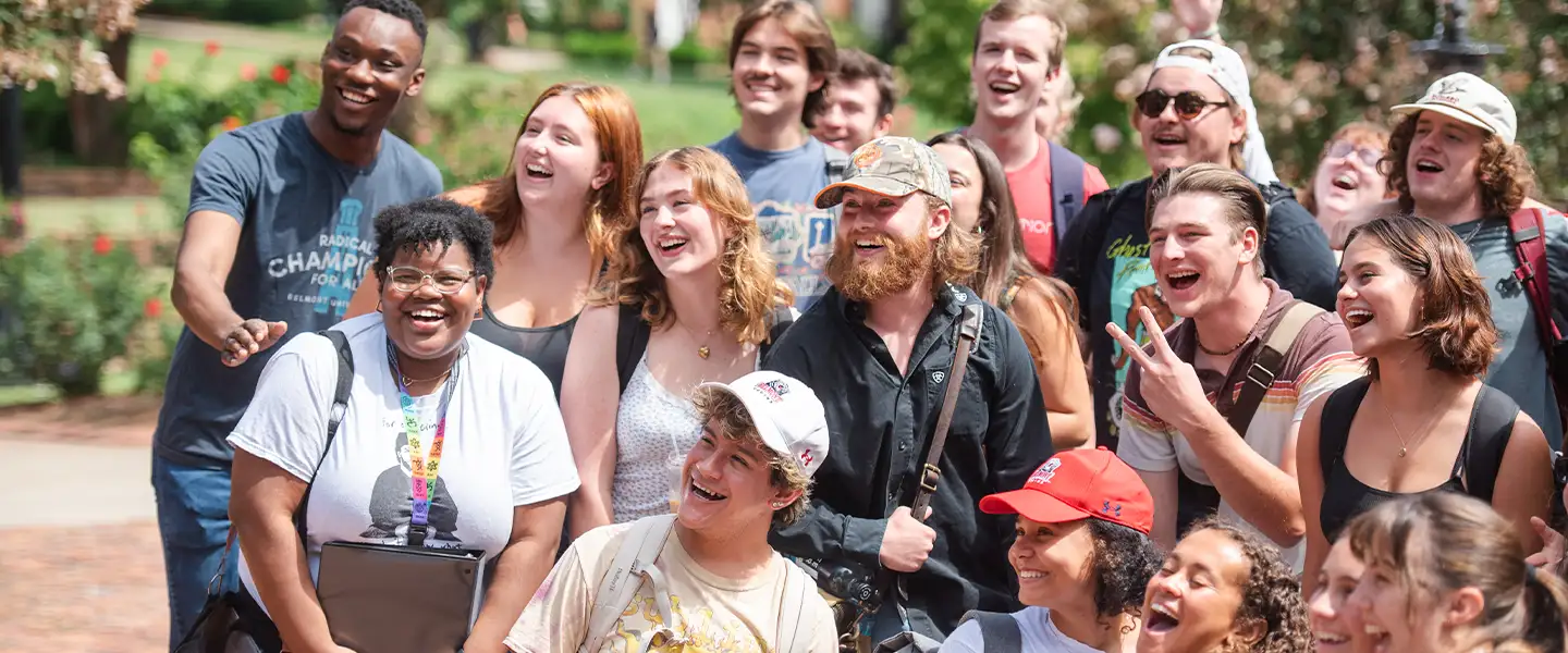 A diverse group of students is gathered outdoors, smiling and laughing together. They are engaged and appear to be enjoying a moment of camaraderie, showcasing the vibrant community spirit at Belmont University.