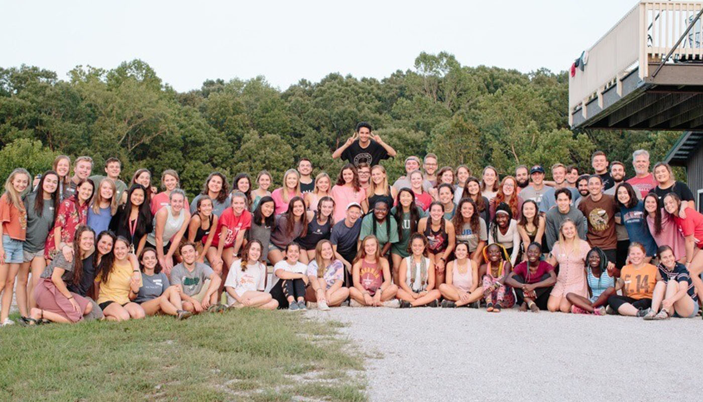 A large group of students poses on a beach.