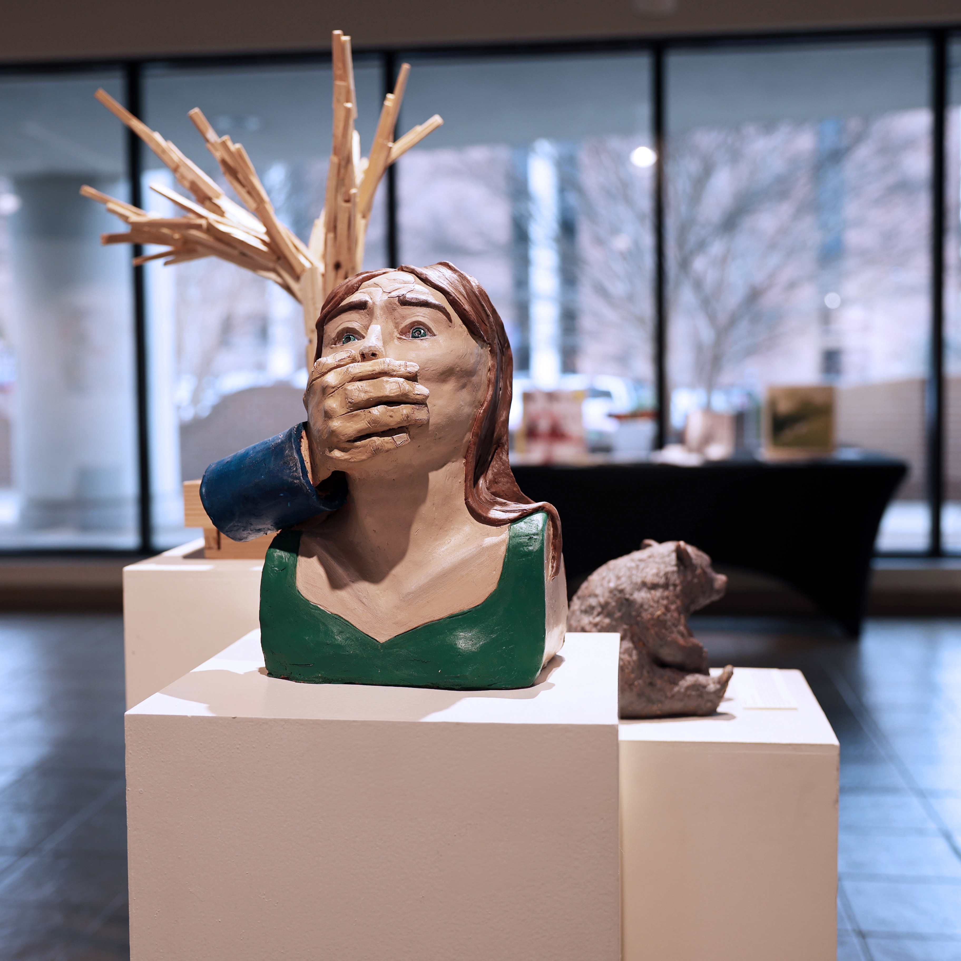 student artwork featuring a wood tree, ceramic bear, and ceramic female bust with hand over mouth