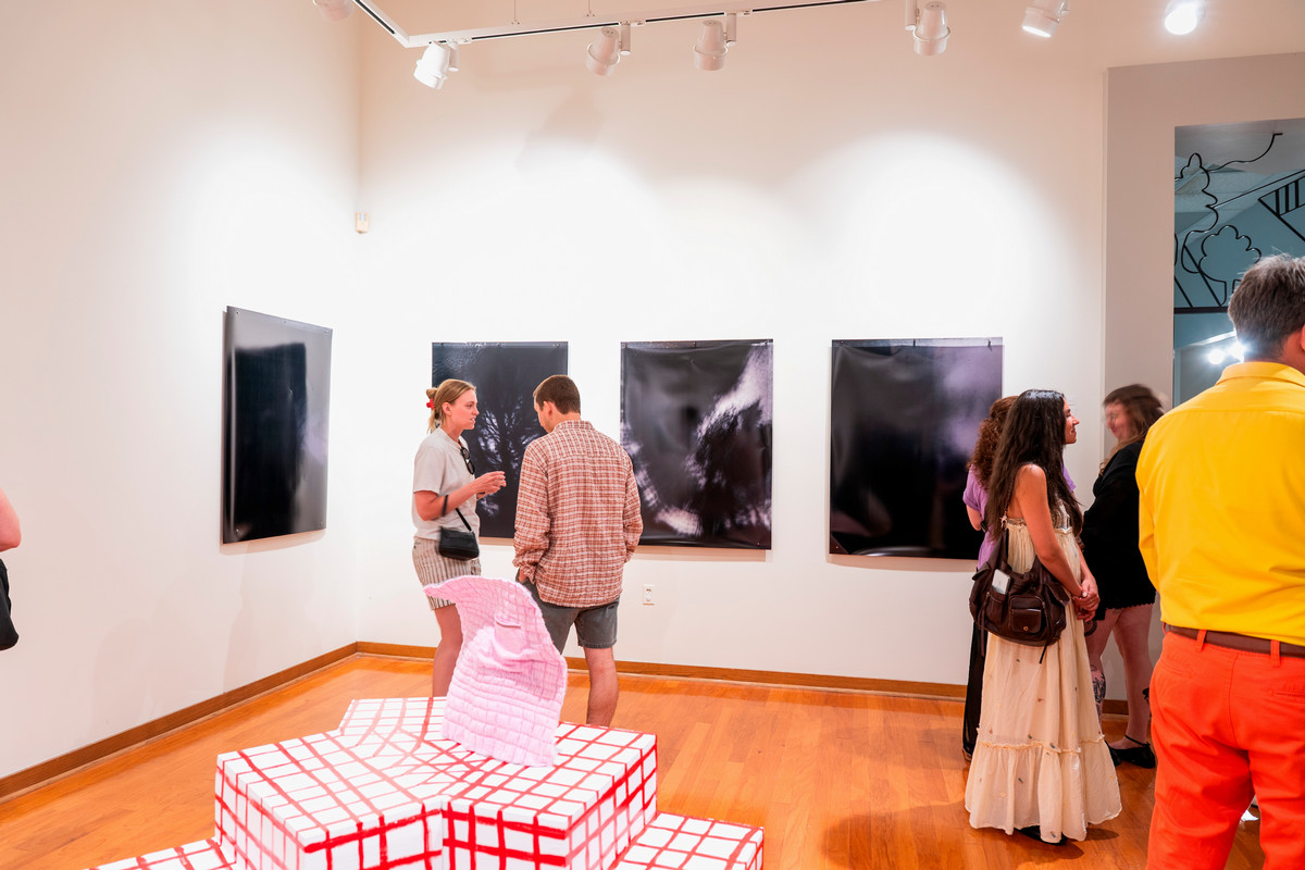 A black-and-white photo of three people sitting close together and smiling in front of a brick wall.
