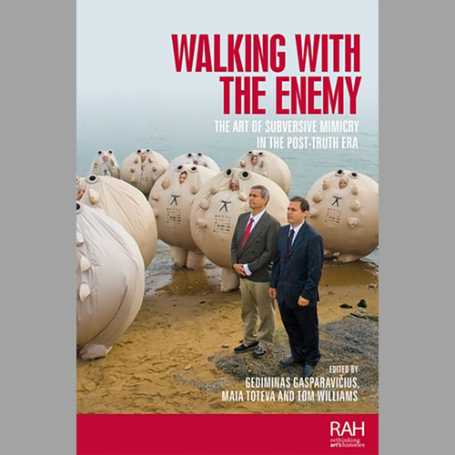Book cover titled Walking with the Enemy: The Art of Subversive Mimicry in the Post-Truth Era. Two people in suits stand on a beach in front of a group of large, rounded sculptural figures. Edited by Gediminas Gasparavicius, Maia Toteva, and Tom Williams.
