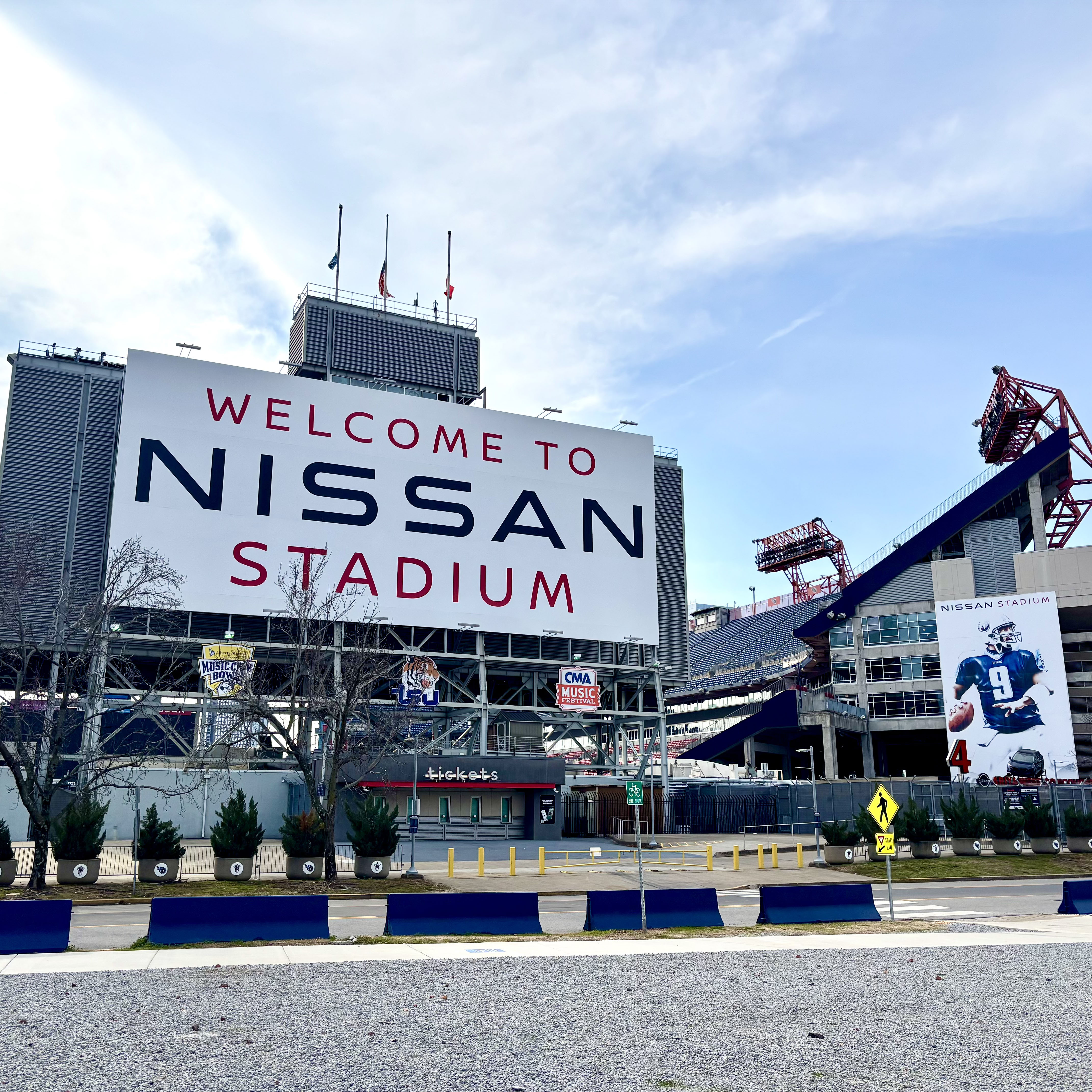 Exterior view of Nissan Stadium with a large "Welcome to Nissan Stadium" sign on the facade under a blue sky.