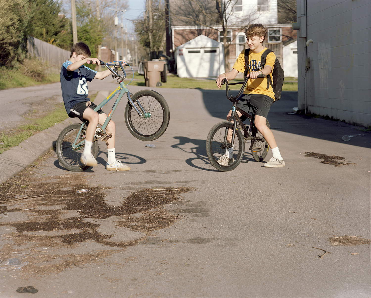 2 boys doing tricks on their bikes in a street