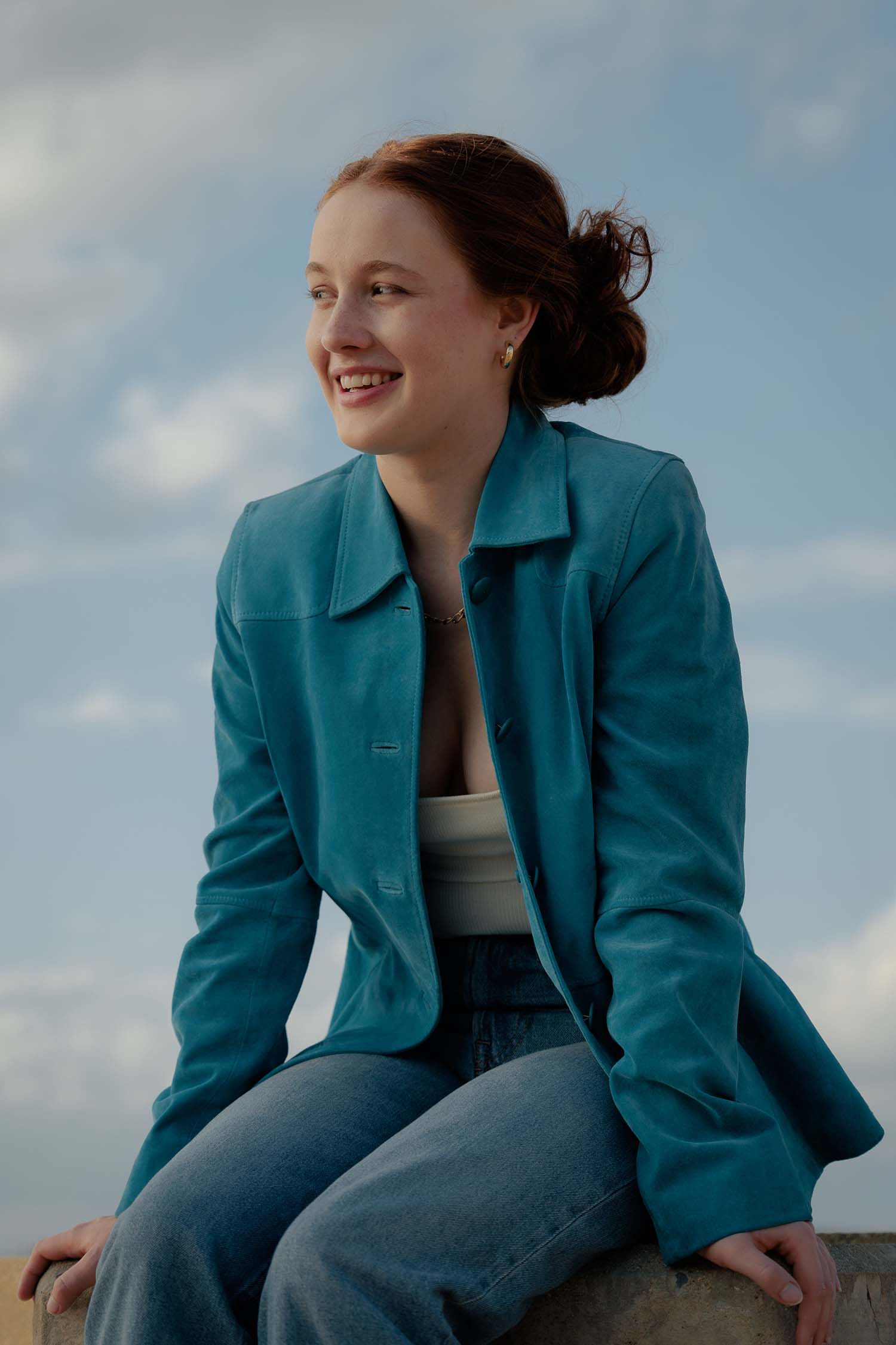 Red headed girl inn blue jacket sitting on a brick wall