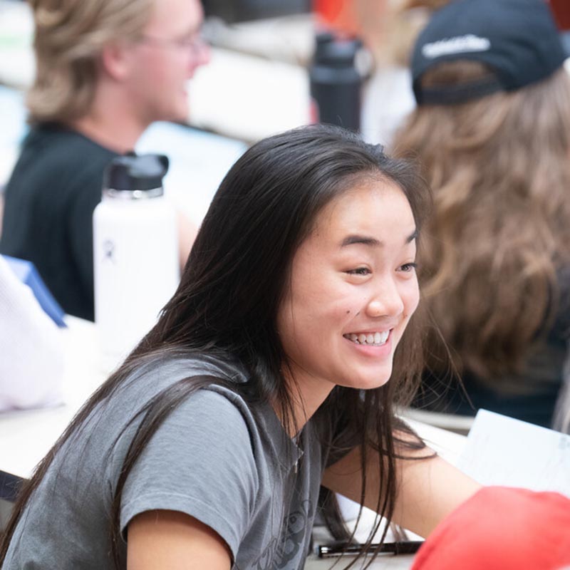 Student laughing in classroom with classmate while talking in small groups